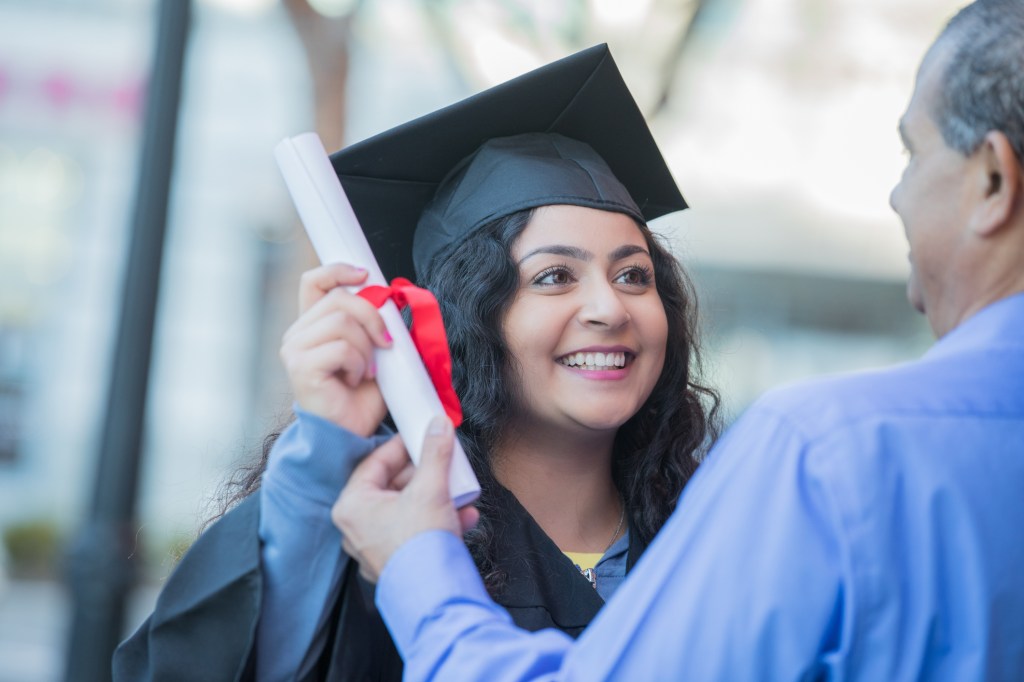 Happy young graduate receiving diploma at outdoor ceremony