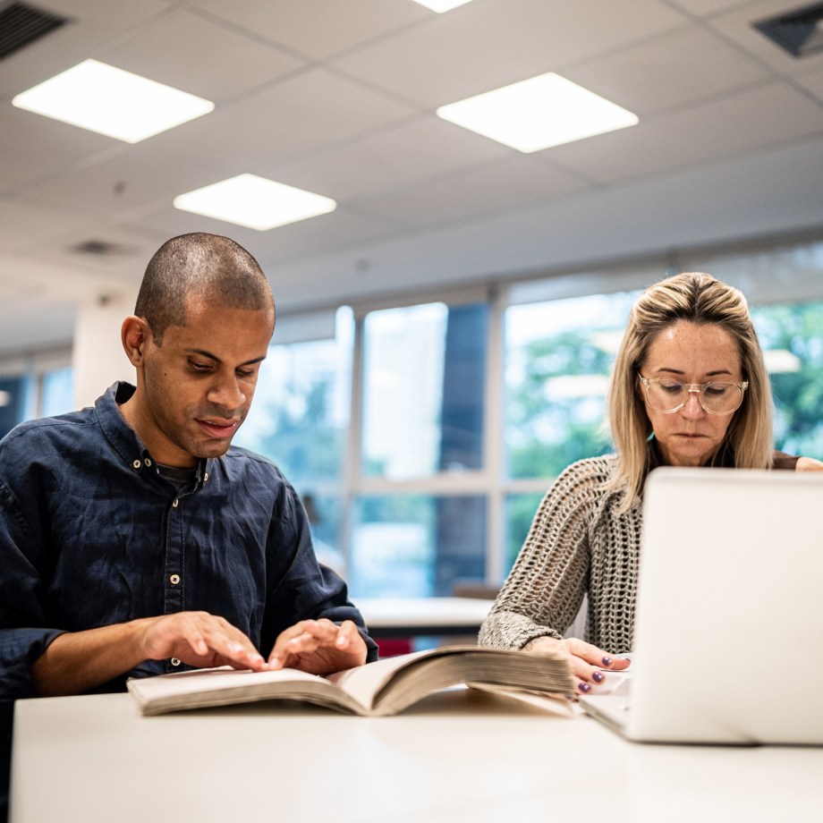 Mid adult man visually impaired man reading a braille book at university