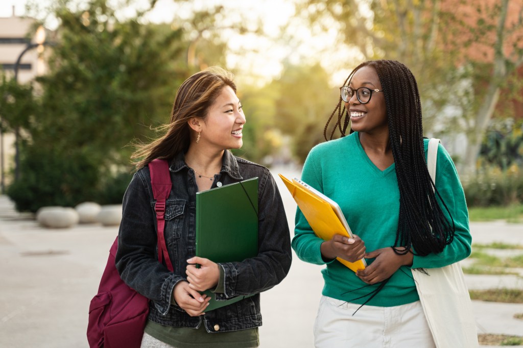 International Asian and African American student girl friends walking after University lecture at sunset