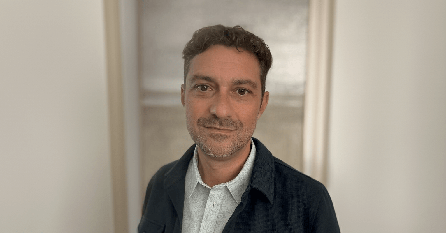 Ken LaOrden, a light-skinned man with brown hair and stubble, wearing a dark blue jacket over a gray collared shirt.